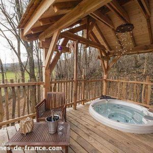 Cabane perchée en Aquitaine avec jacuzzi sur une terrasse en bois, vue sur la nature.