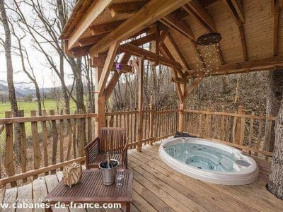 Cabane perchée en Aquitaine avec jacuzzi sur une terrasse en bois, vue sur la nature.