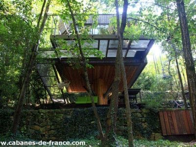 Cabane perchée en bois, suspendue entre les arbres, offrant une vue sur la nature verdoyante.