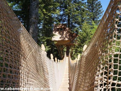 Cabane perchée en Auvergne, accessible par un pont suspendu en bois.