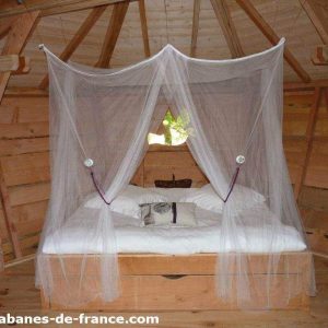 Cabane en bois avec lit à baldaquin et moustiquaire, ambiance cosy et naturelle.