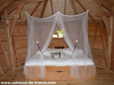 Cabane en bois avec lit à baldaquin et moustiquaire, ambiance cosy et naturelle.