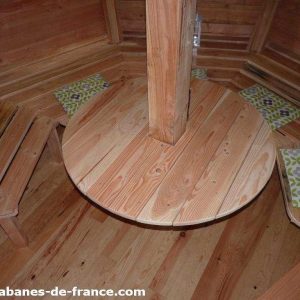Cabane en bois avec un intérieur chaleureux et une table ronde centrale.