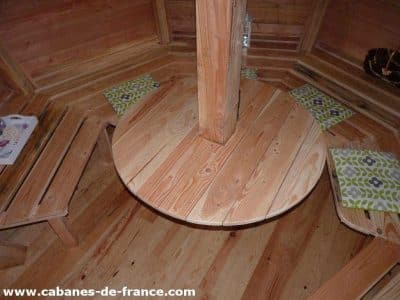 Cabane en bois avec un intérieur chaleureux et une table ronde centrale.