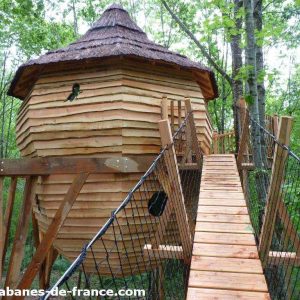 Cabane perchée en bois dans les arbres, accessible par un pont suspendu.