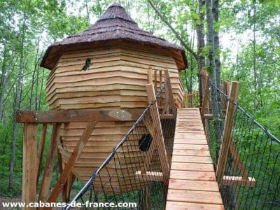 Cabane perchée en bois dans les arbres, accessible par un pont suspendu.