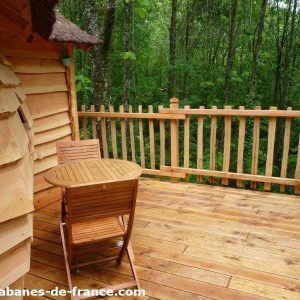 Cabane en bois perchée, avec terrasse en bois et vue sur la forêt verdoyante.