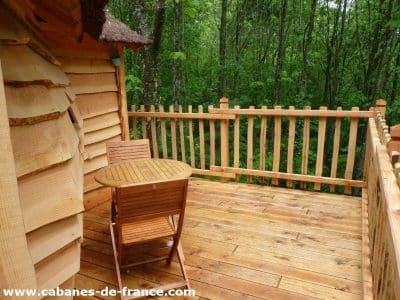Cabane en bois perchée, avec terrasse en bois et vue sur la forêt verdoyante.
