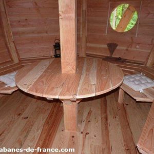 Cabane en bois avec table centrale et bancs, ambiance chaleureuse et naturelle.