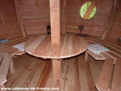 Cabane en bois avec table centrale et bancs, ambiance chaleureuse et naturelle.