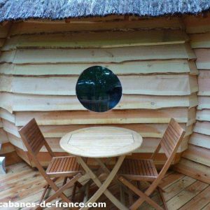 Cabane en bois avec toit de chaume et fenêtre ronde, idéale pour un séjour unique.
