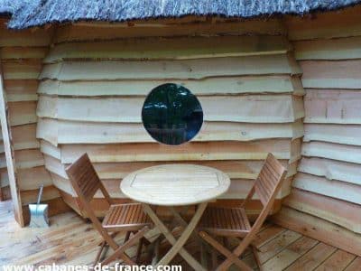 Cabane en bois avec toit de chaume et fenêtre ronde, idéale pour un séjour unique.