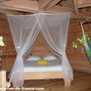 Cabane en bois en Aquitaine, lit double avec rideaux légers et hamac suspendu.