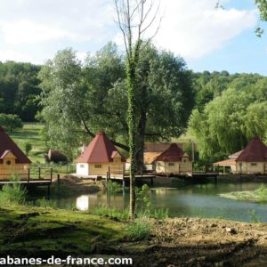 Cabanes en bois au bord dun étang, entourées de verdure et de nature paisible.