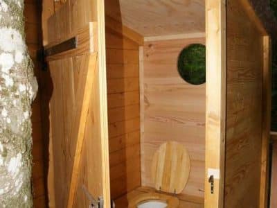 Cabane en bois perchée, avec toilettes écologiques et vue sur la nature environnante.