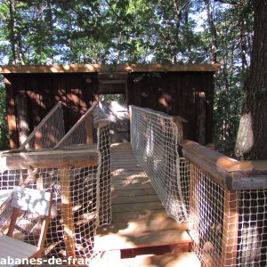 Cabane perchée dans les arbres, accessible par un pont en bois et filet.