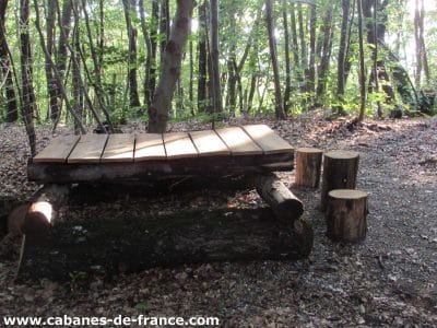 Cabanes en bois dans les bois, avec une plateforme et des troncs comme sièges.