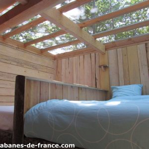 Cabane en bois avec lit confortable et toit vitré, vue sur la nature.