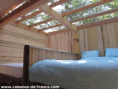 Cabane en bois avec lit confortable et toit vitré, vue sur la nature.