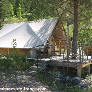 Tente safari en bois sur pilotis, entourée de verdure en Auvergne-Rhône-Alpes.