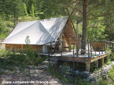Tente safari en bois sur pilotis, entourée de verdure en Auvergne-Rhône-Alpes.