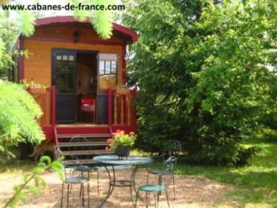 Charmante roulotte en bois entourée darbres, avec une terrasse et une table.