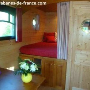 Cabane en bois cosy avec lit rouge et décoration chaleureuse, idéale pour un séjour unique.