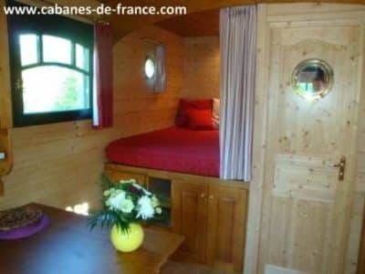 Cabane en bois cosy avec lit rouge et décoration chaleureuse, idéale pour un séjour unique.