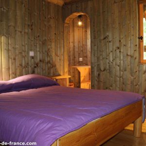 Cabane en bois à Nouvelle-Aquitaine, lit double avec draps violets et murs en bois.