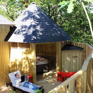 Cabane en bois avec jacuzzi, entourée de verdure, idéale pour un séjour relaxant.