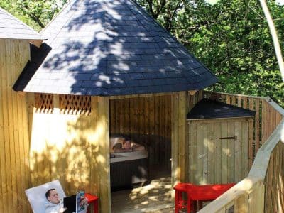 Cabane en bois avec jacuzzi, entourée de verdure, idéale pour un séjour relaxant.