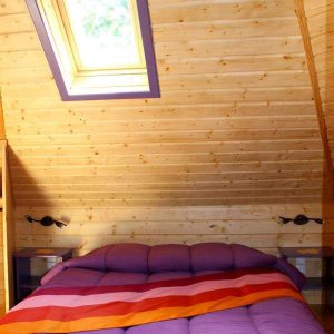 Cabanes en bois en Nouvelle-Aquitaine, lit coloré sous un puits de lumière.