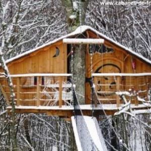Cabane dans les arbres en bois, entourée de neige, offrant une vue paisible.