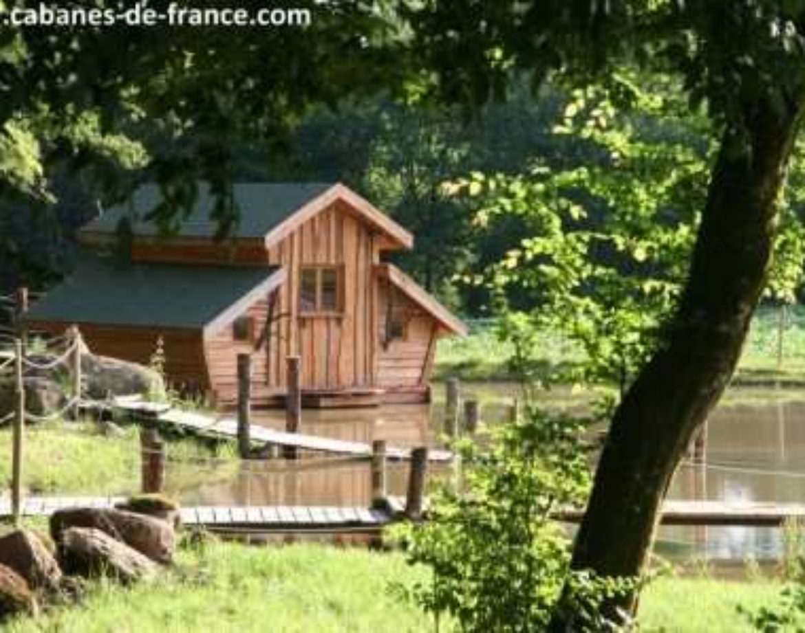 Cabane en bois flottant entourée darbres, au bord dun étang paisible.