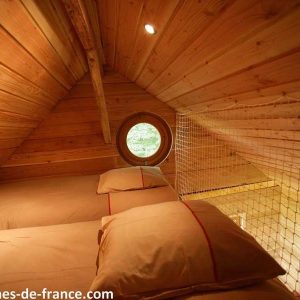 Cabane en bois à Champagne-Ardennes, avec lits douillets et fenêtre ronde.