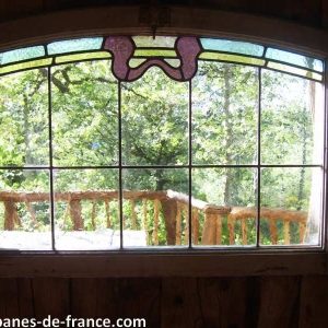 Vue depuis une cabane perchée dans les arbres, avec un vitrail coloré.