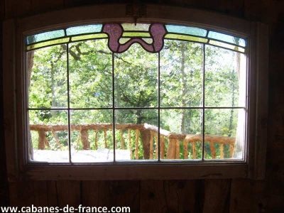 Vue depuis une cabane perchée dans les arbres, avec un vitrail coloré.