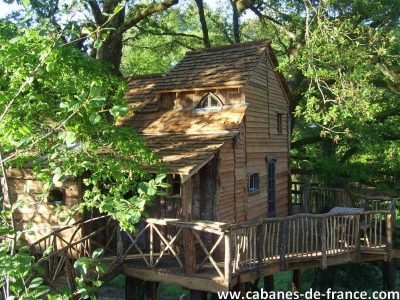 Cabane dans les arbres à Limousin, entourée de verdure et avec une terrasse en bois.