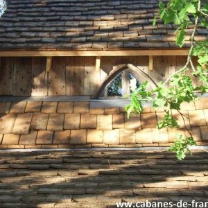 Cabane en bois au Limousin, avec un toit en bardeaux et une fenêtre en arc.