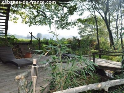 Cabane perchée dans les arbres, entourée de verdure et dun pont en bois.