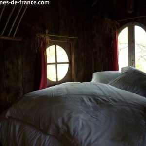 Cabane en bois à Limousin, lit douillet sous des fenêtres rondes.