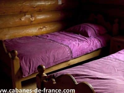 Chalet en bois en Auvergne avec lits jumeaux et draps violets. Ambiance chaleureuse.