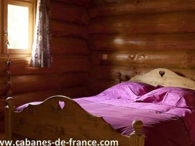 Chalet en bois avec lit en bois sculpté et draps violets, ambiance chaleureuse.