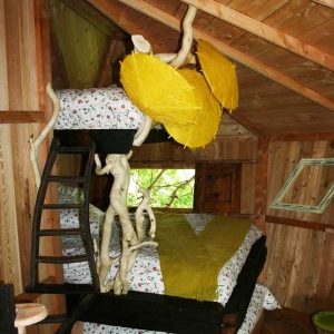 Cabane perchée en bois avec lits colorés et décor naturel, ambiance chaleureuse.
