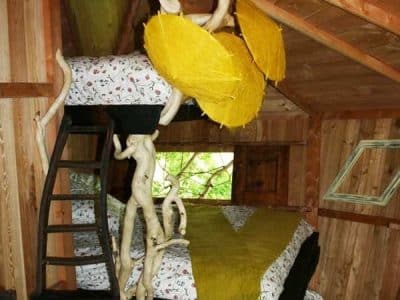 Cabane perchée en bois avec lits colorés et décor naturel, ambiance chaleureuse.