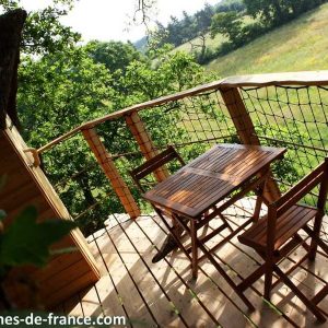 Cabane perchée en bois avec terrasse en bois et vue sur la nature verdoyante.
