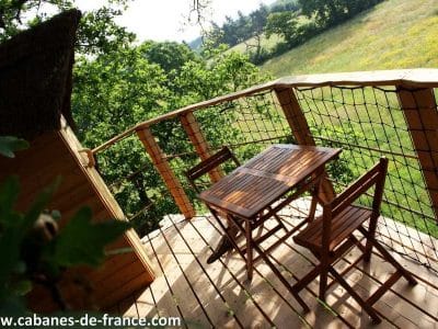 Cabane perchée en bois avec terrasse en bois et vue sur la nature verdoyante.
