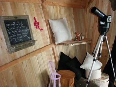 Cabane en bois cosy avec un télescope et des coussins confortables.