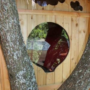 Cabane perchée dans un arbre avec une fenêtre ronde et un décor en bois naturel.
