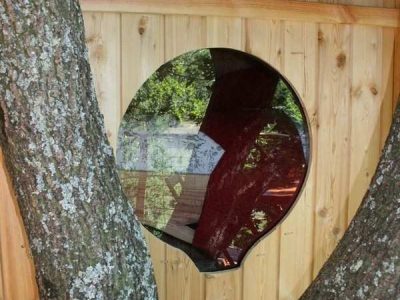 Cabane perchée dans un arbre avec une fenêtre ronde et un décor en bois naturel.